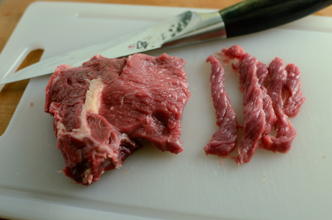 A chunk of beef is thinly sliced into long strips.
