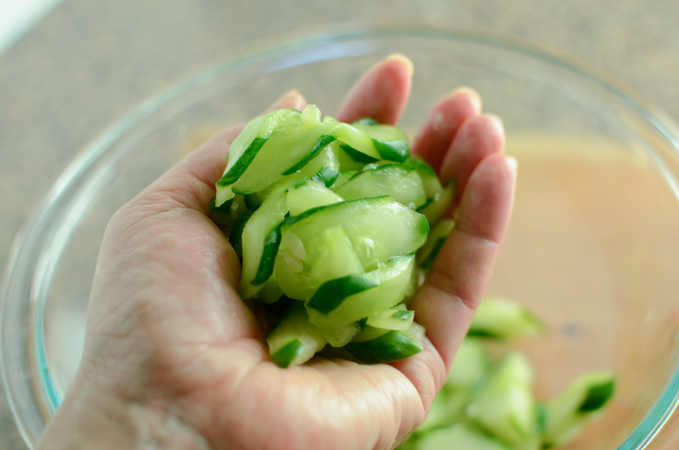 Salted cucumber slices are being squeezed out to remove excess water.