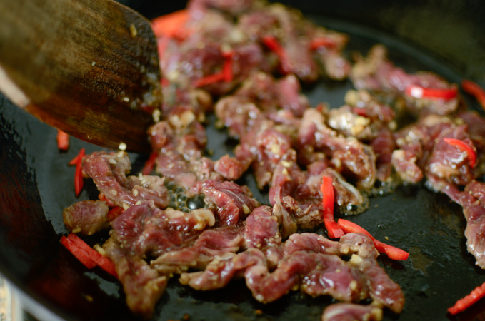 Beef strips are stir frying with chili slices in a skillet.