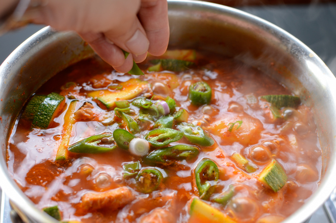 Chopped green onion is sprinkled on spicy tuna potato stew in a pot.