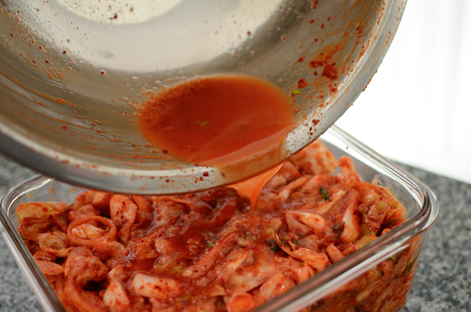 Pouring the extra water from the kimchi mixing bowl into the freshly made kimchi.