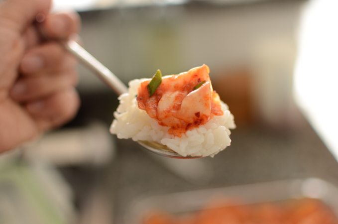 A piece of green cabbage kimchi is placed on top of a spoonful of rice.