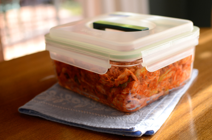 Green cabbage kimchi is stored in an air-tight glass container for fermentation.