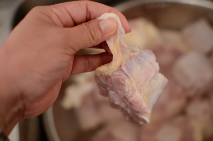 A hand is holding extra fat and skin from an ox tail bone.