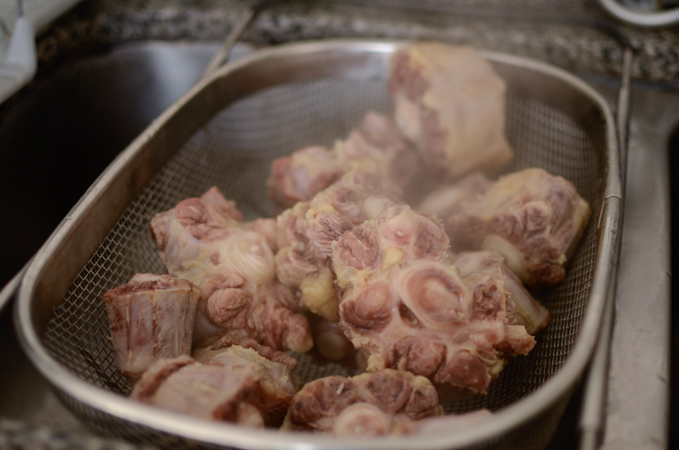 Boiled ox tail bones are drained through a colander.