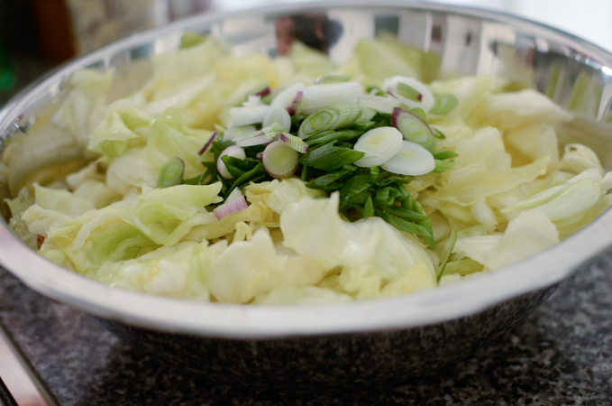 Drained cabbage pieces and green onion are combined  in a mixing bowl.