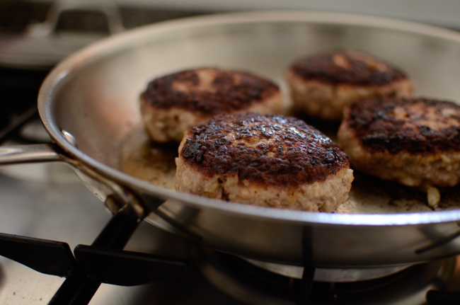 Hamburger steak patties are browning in a skillet.