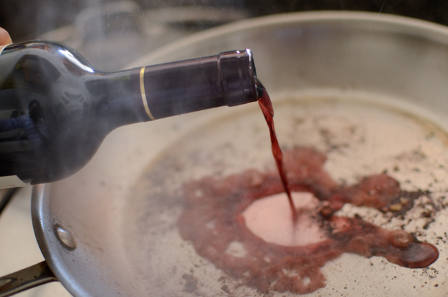 Red wine is poured on a hot skillet to deglaze the meat dripping.