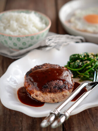 Hambagu is drizzled with red wine sauce and served with rice and spinach.