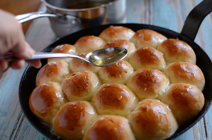 A spoonful of honey syrup is being pour over hot beehive buns in a skillet.