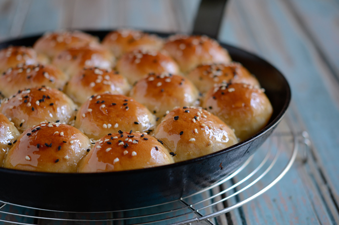 Sesame seeds and black sesame seeds are sprinkled on top of beehive buns in a skillet.