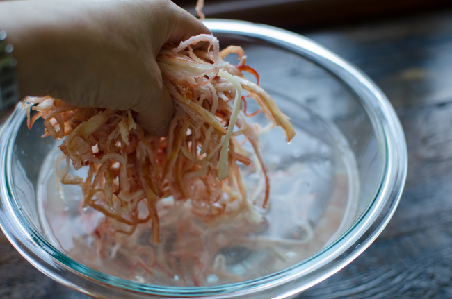 Shredded squids are removed from the soaking water in a bowl.