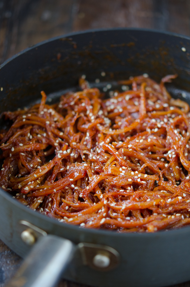 Korean shredded squid side dish is garnished with sesame seeds in a skillet.