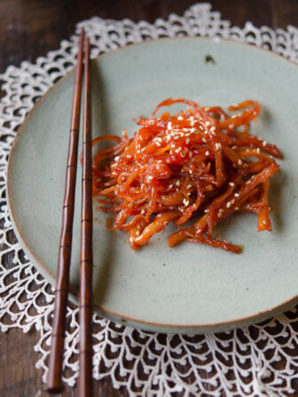 Korean shredded squid side dish is on a greet plate with a pair of chopsticks.