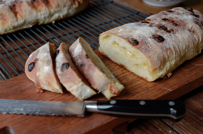 Club Med White Chocolate Bread is sliced with a bread knife on a wooden board.