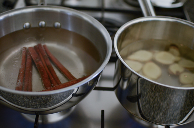 Cinnamon sticks and ginger slices are simmering in  separate pots.