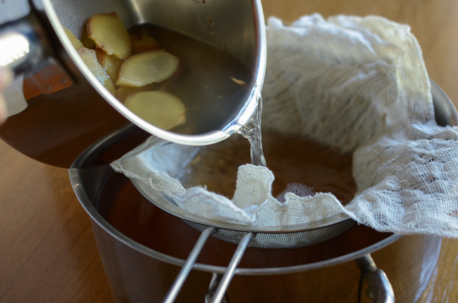 Ginger water is strained in a kitchen clothe over a strainer.