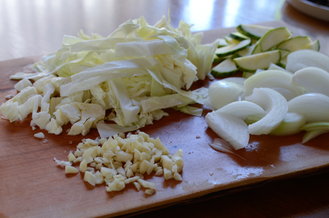 Cabbage, onion, zucchini and garlic is chopped on the cutting board.