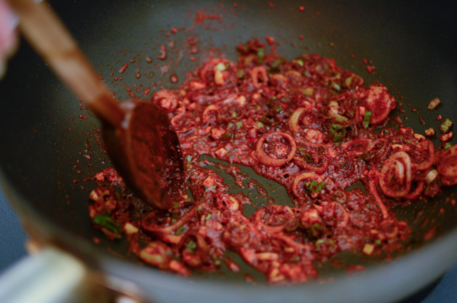 Korean chili flakes are added and mixed with green onion in a wok.