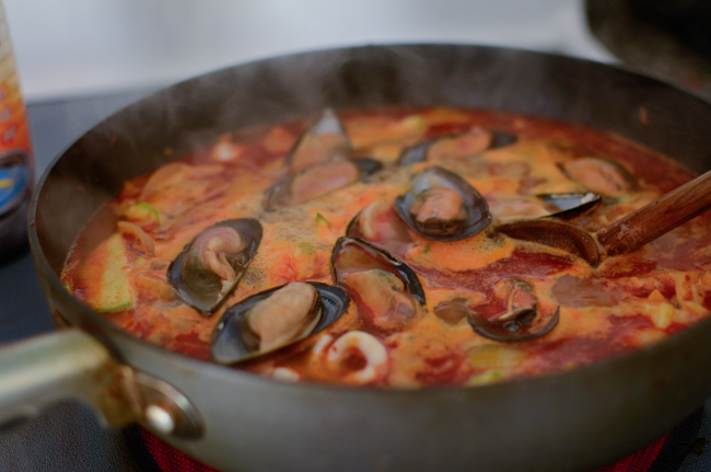Shelled mussel are added to the spicy soup in a wok.