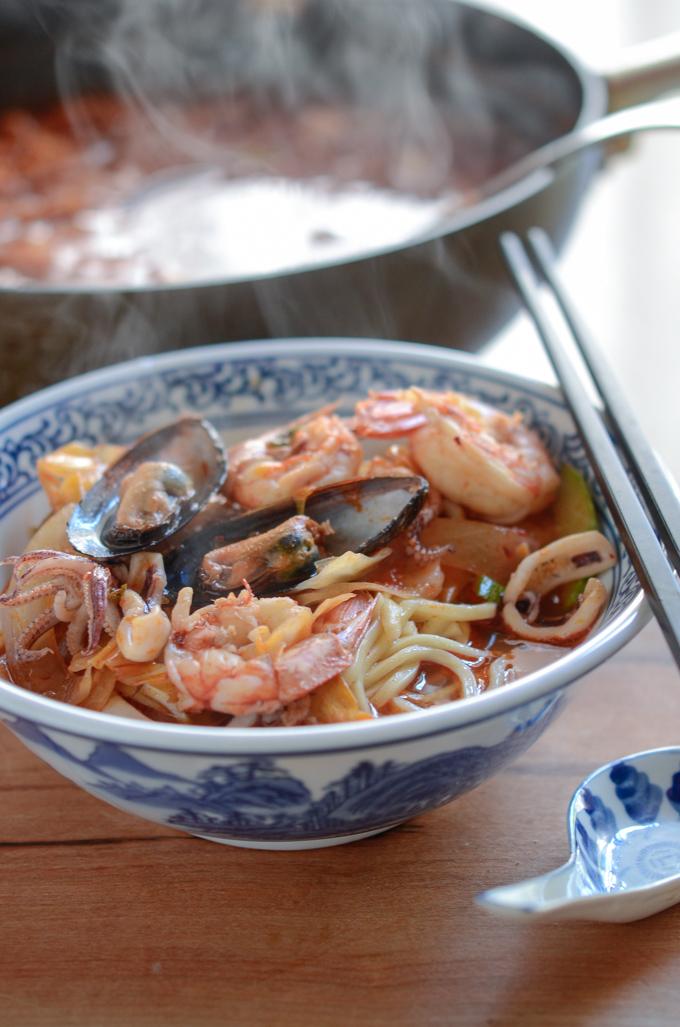 A bowl of jjamppong is served steaming hot in a bowl with a ton of seafood.