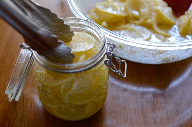 Lemon sugar mixture is put into a glass jar using a kitchen tong.