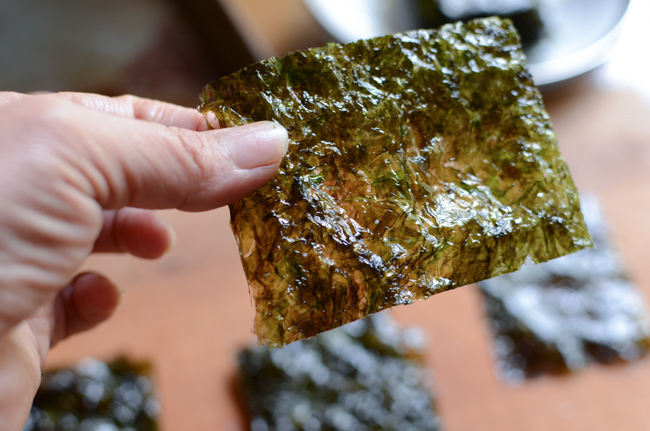 A hand is holding a thin piece of roasted seaweed snack.