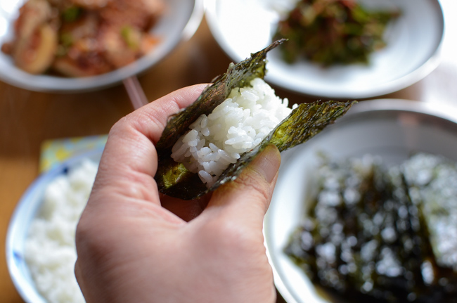 A hand is holding rice wrapped in a piece of roasted seaweed snack.