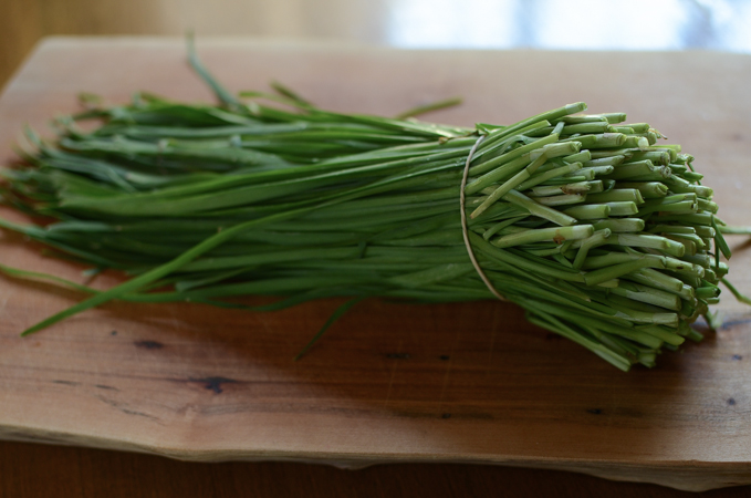 A bunch of garlic chives are placed on a cutting board.