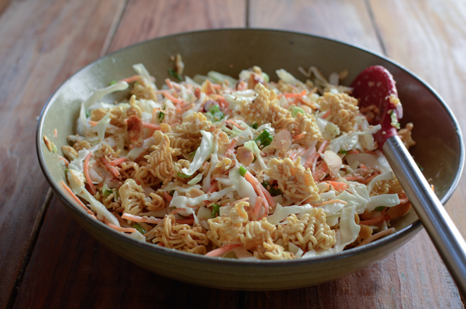 Cabbage ramen noodle salad is tossed with salad dressing in a mixing bowl.