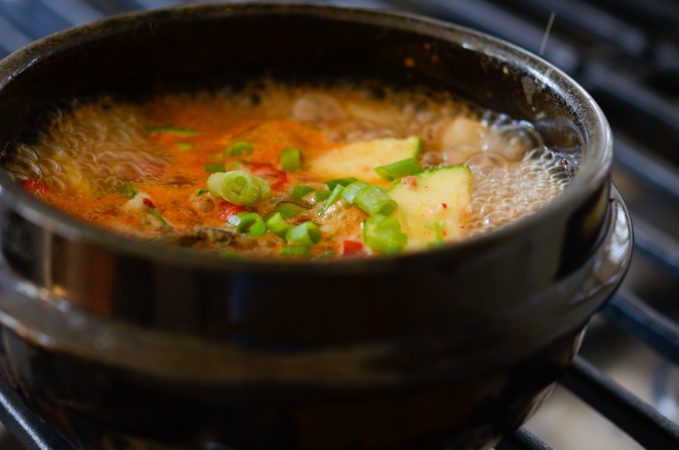 Korean soybean paste stew is boiling on a stove to serve with turnip kimchi.