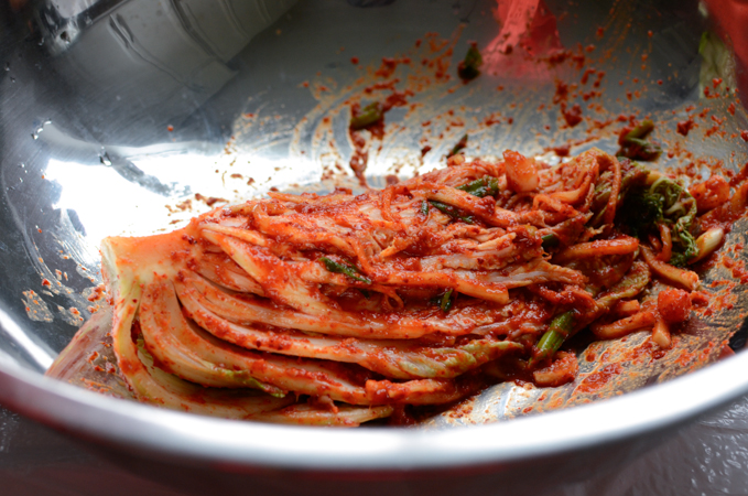 A head of cabbage is rubbed with kimchi paste inside a mixing bowl.