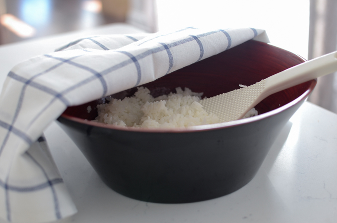 A kitchen cloth is covering the sushi rice in a wooden bowl.