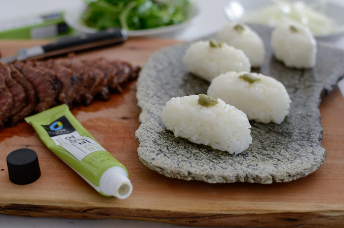 A tube of wasabi is topping the sushi rice on a stone platter.