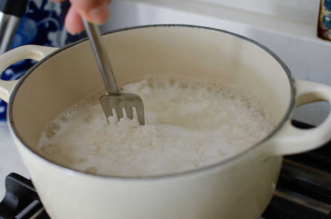 A fork is stirring the simmering rice in a pot.