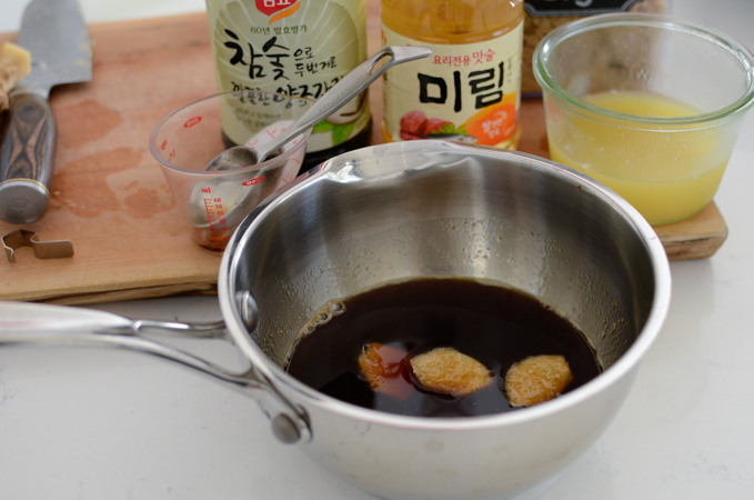 Teriyaki sauce ingredients are combined in a sauce pan with two slices of ginger.