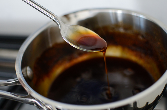 A spoon is drizzling teriyaki sauce over the sauce pan to show the consistency.