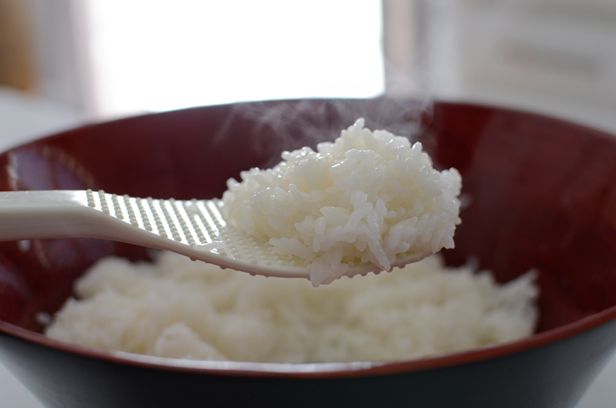 A rice scoop is holding a steaming portion of seasoned sushi rice.