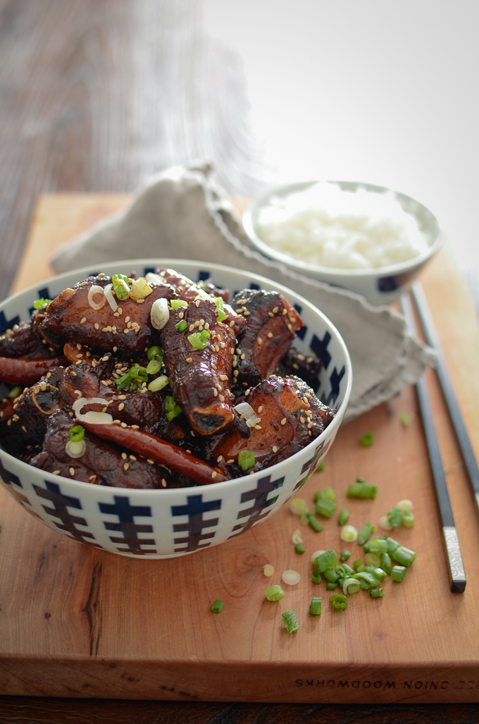 Stickly Chinese sweet and sour pork ribs are garnished and served with rice and chopsticks.