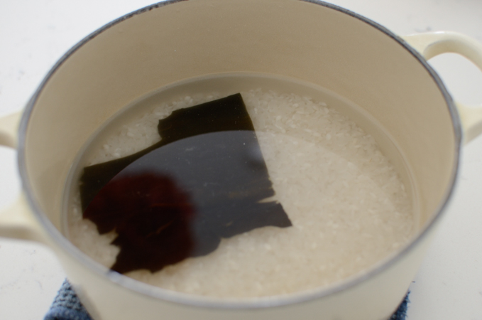 Rice is soaking in water with a piece of sea kelp in a pot.