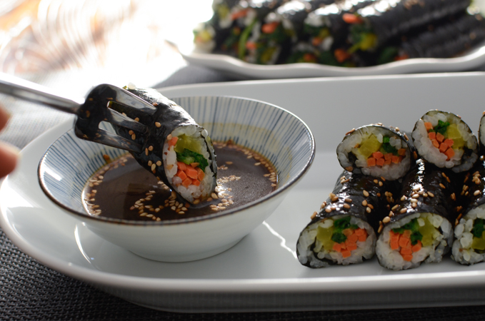 A fork is dipping a mini seaweed roll into the dipping sauce.