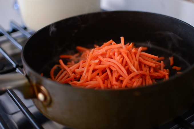 Shredded carrots are added to a skillet to cook.