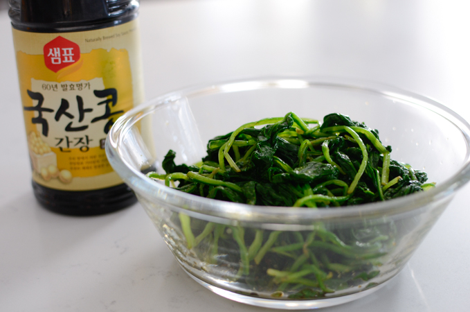 Blanched spinach is seasoned with Korean soy sauce in a glass bowl.