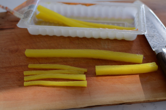 Pickled radish is sliced into small strips on the cutting board.