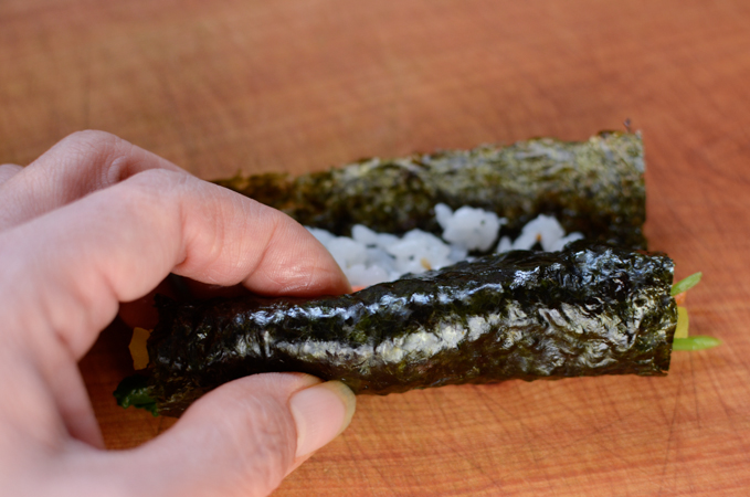 A hand is rolling mini seaweed rolls to wrap tightly.