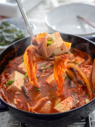 A ladle of anchovy kimchi stew and toful in a pot is ready to serve