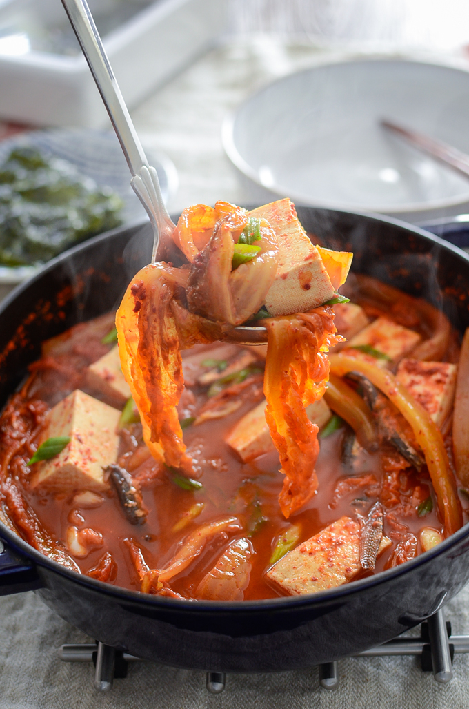 A ladle of anchovy kimchi stew and toful in a pot is ready to serve.