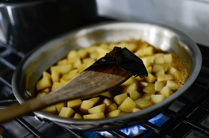 A piece of sea kelp is removed by a wooden spatula from a skillet with potato and sauce.