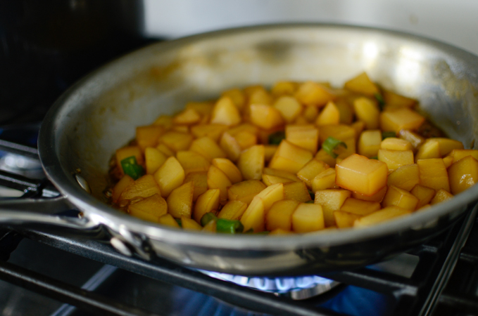 Potato cubes are cooking in a soy sauce mixture in a skillet.