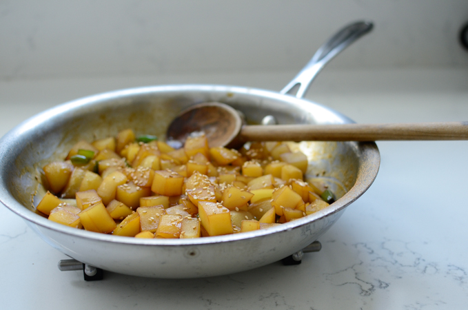 Korean braised potatoes are garnished with sesame seeds in a skillet.